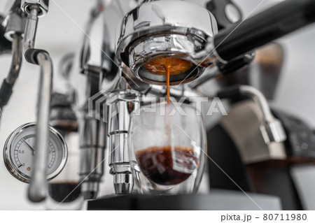 Coffee machine pouring single shot espresso in double wall glass from bottomless naked portafilter. Professional equipment at home or cafe Coffee machine pouring single shot espresso in double wall glass from bottomless naked portafilter. Professional equipment at home or cafe 80711980