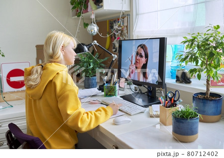 Teenager girl sitting at home studying online using home computer. 80712402