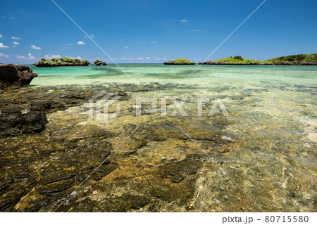 Gorgeous crystalline emerald green sea over a coastal rocks platform, blue sky, green islets in the background. Iriomote Island. 80715580