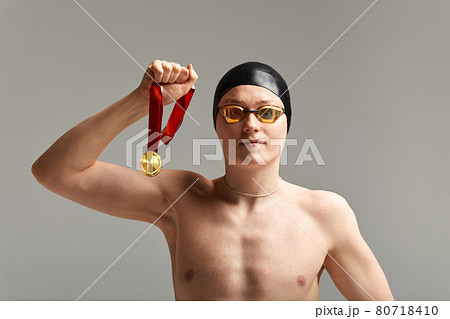 Swimmer with a medal on a gray background rejoices in victory, an athlete in excellent physical shape celebrates a victory clutching a medal in his hand, victory concept, gray background, copy space Swimmer with a medal on a gray background rejoices in victory, an athlete in excellent physical shape celebrates a victory clutching a medal in his hand, victory concept, gray background, copy space 80718410