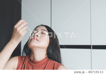 Patient asian woman doing a nasal swab self test rapid antigen testing kit for checking a covid-19 at home Patient asian woman doing a nasal swab self test rapid antigen testing kit for checking a covid-19 at home 80719113