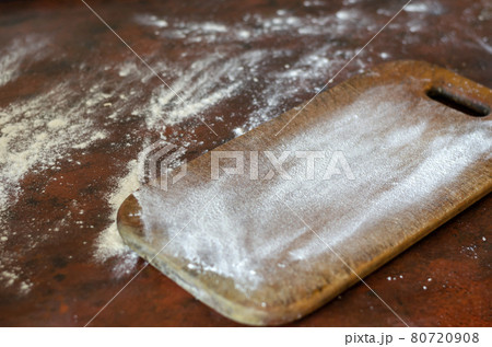 A kitchen table with a wooden cutting board is covered in flour. A kitchen table with a wooden cutting board is covered in flour. 80720908