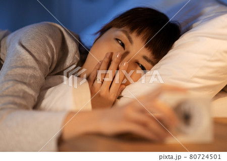 asian woman with clock yawning in bed at night asian woman with clock yawning in bed at night 80724501
