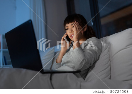 woman with laptop calling on phone in bed at night woman with laptop calling on phone in bed at night 80724503