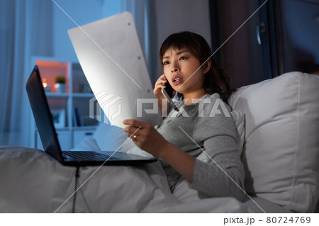 woman with laptop calling on phone in bed at night woman with laptop calling on phone in bed at night 80724769