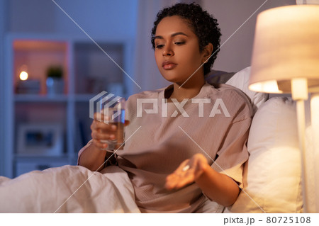 woman with medicine and water in bed at night 80725108