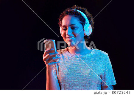 woman in headphones with smartphone in neon lights 80725242