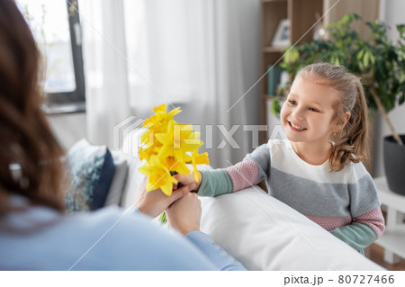 happy daughter giving daffodil flowers to mother 80727466
