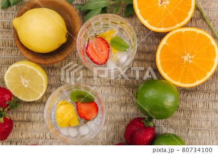 Top view of two tall glasses with water ice and strawberry. Slices fresh fruits on the table outdoor. Lime lemon and orange. Food concept 80734100