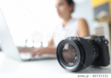 Black professional camera lying on background of woman laptop closeup Black professional camera lying on background of woman laptop closeup 80735332