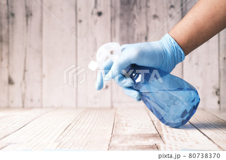 hand in blue rubber gloves holding spray bottle cleaning table  80738370