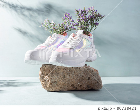 White sneakers with purple flowers on turquoise on stone podium 80738421