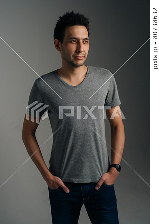 Vertical portrait of confident young man in gray T-shirt standing with with hands in pockets on dark isolated background. Vertical portrait of confident young man in gray T-shirt standing with with hands in pockets on dark isolated background. 80738632