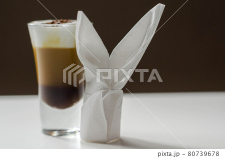 Coffee drink shot with a nutty note with fluffy milk foam, decorated with chocolate shavings, served with an Easter bunny-shaped napkin 80739678