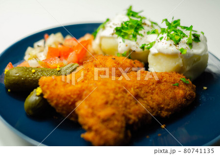 Breaded and herbed chicken breast fillet served with mashed potatoes,  tomato salad with onions and gherkin 80741135