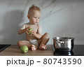 little boy sits on the kitchen countertop with green apples 80743590