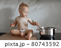little boy in the kitchen is stirring soup in a saucepan 80743592