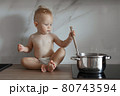 little boy in the kitchen is stirring soup in a saucepan 80743594