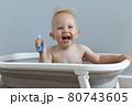 laughing small child rushes his teeth while sitting in the bathroom 80743605