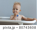 A small child rushes his teeth while sitting in the bathroom 80743608