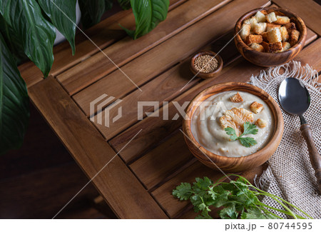 White cauliflower cream soup with croutons , spoon and herbs on brown table 80744595