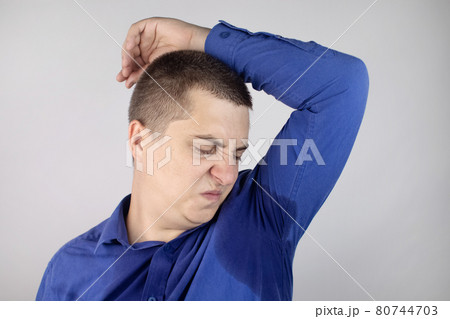 The man shows his sweaty armpits to the camera. Close-up of sweat drops. Gland problems. Hyperhidrosis, increased sweating, anhidrosis. Concept of treatment for violations of the mechanisms secretion. 80744703
