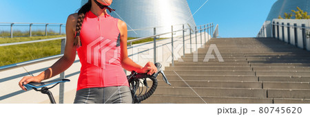 Road cycling in city cyclist athlete woman with bike wearing pink jersey outfit for sports biking on summer urban commute ride. Bicycle concept panoramic background Road cycling in city cyclist athlete woman with bike wearing pink jersey outfit for sports biking on summer urban commute ride. Bicycle concept panoramic background 80745620