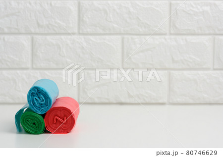 stack of disposable plastic trash can bags on white table, white brick wall background 80746629
