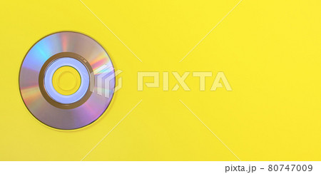 Top down view, small CD shiny / rainbow side, on yellow board, space for text on right side. 80747009