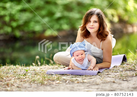 Young mother with baby of 4 months is resting in park on mat. 80752143