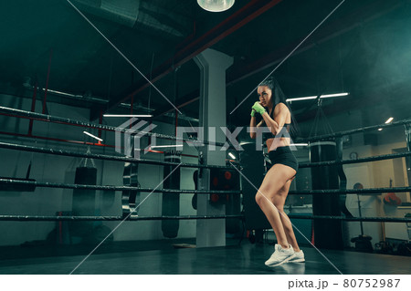 Athletic woman standing on boxing ring prepared for fight with boxing bandages on hands Athletic woman standing on boxing ring prepared for fight with boxing bandages on hands 80752987