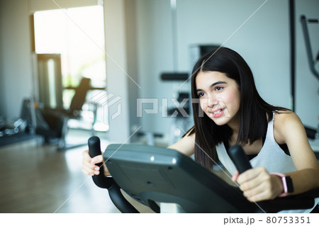 Fit young girl using exercise bike at the gym. Fitness female using air bike at gym. 80753351