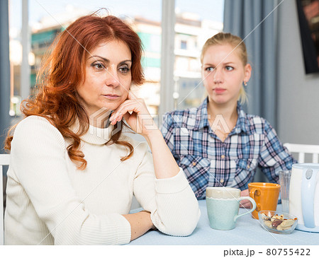 Mature female talking with young daughter at table in home Mature female talking with young daughter at table in home 80755422