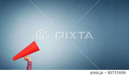 Hand of woman holding paper trumpet against concrete background Hand of woman holding paper trumpet against concrete background 80755606