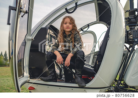 Confident preteen girl in camo style blouse sitting in open helicopter 80756628