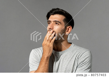 Shocked young Caucasian man looking up and thinking with hand cover mouth  80757403