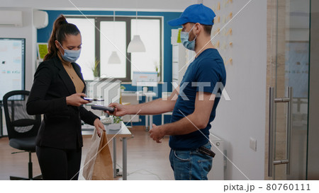 Businesswoman with face mask against coronavirus paying takeaway food order with contactless phone 80760111