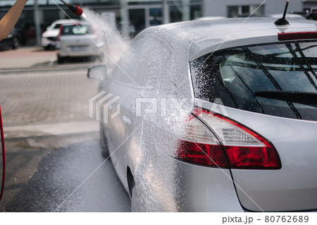 Back view of young woman cleaning her car on self service car. Female washing with jet sprayer. White foam on car Back view of young woman cleaning her car on self service car. Female washing with jet sprayer. White foam on car 80762689