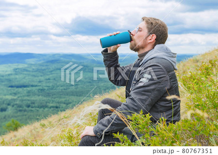A man in a gray jacket on a mountain top drinks water from a bottle. Close up. A man in a gray jacket on a mountain top drinks water from a bottle. Close up. 80767351