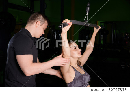 The coach helps the girl to perform exercises on the simulator. The coach helps the girl to perform exercises on the simulator. 80767353