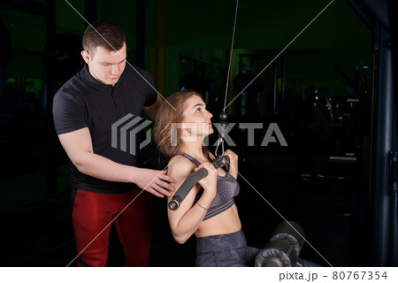 The coach helps the girl to perform exercises on the simulator. The coach helps the girl to perform exercises on the simulator. 80767354