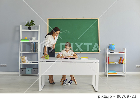 Friendly school teacher helping little pupil with math assignment in modern classroom Friendly school teacher helping little pupil with math assignment in modern classroom 80769723