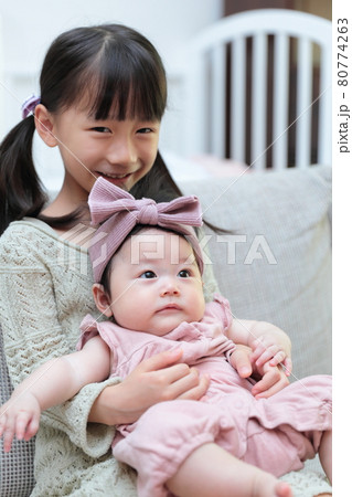 ソファに抱っこして座る赤ちゃんと幼児の仲良しの姉妹 ソファに抱っこして座る赤ちゃんと幼児の仲良しの姉妹 80774263