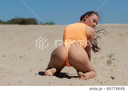 Seductive model in swimsuit kneeling on sandy beach 80776688
