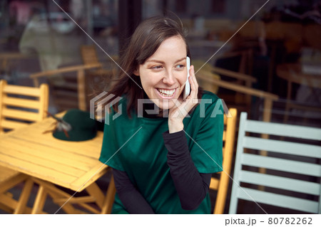 Portrait of cheerful young caucasian woman in green clothes that sitting outside cafe 80782262