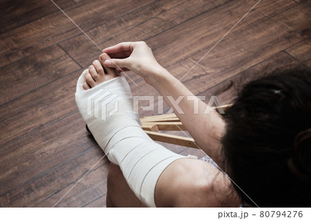 A woman massages the toes of a broken leg with her hands. Top view of a broken leg in a plaster cast and crutches. Home rehabilitation after a broken leg. High quality photo A woman massages the toes of a broken leg with her hands. Top view of a broken leg in a plaster cast and crutches. Home rehabilitation after a broken leg. High quality photo 80794276