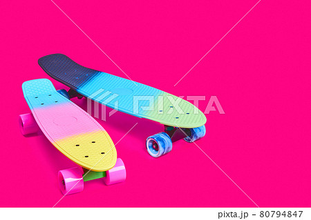 Two rainbow plastic Penny board skateboards on crimson background 80794847