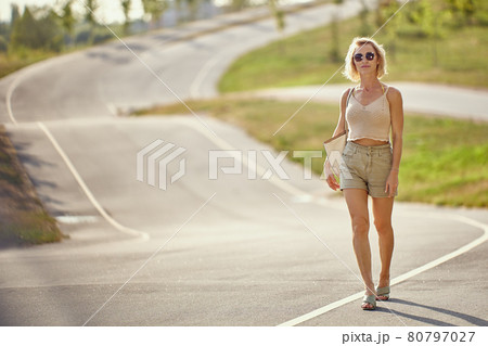 Graceful blond woman walks on empty road. 80797027