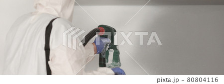 Master painter in white suit paints wall with a spray gun 80804116