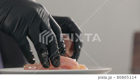 man hands spreading marinade over raw turkey fillet slices in white bowl 80805114